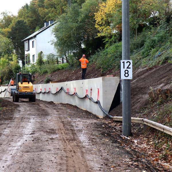 Ein Bagger fährt entlang der Stützmauer. Die Gleise in dem Bereich der Erfttalbahn fehlen. Auf der Mauer steht ein Arbeiter und telefoniert.