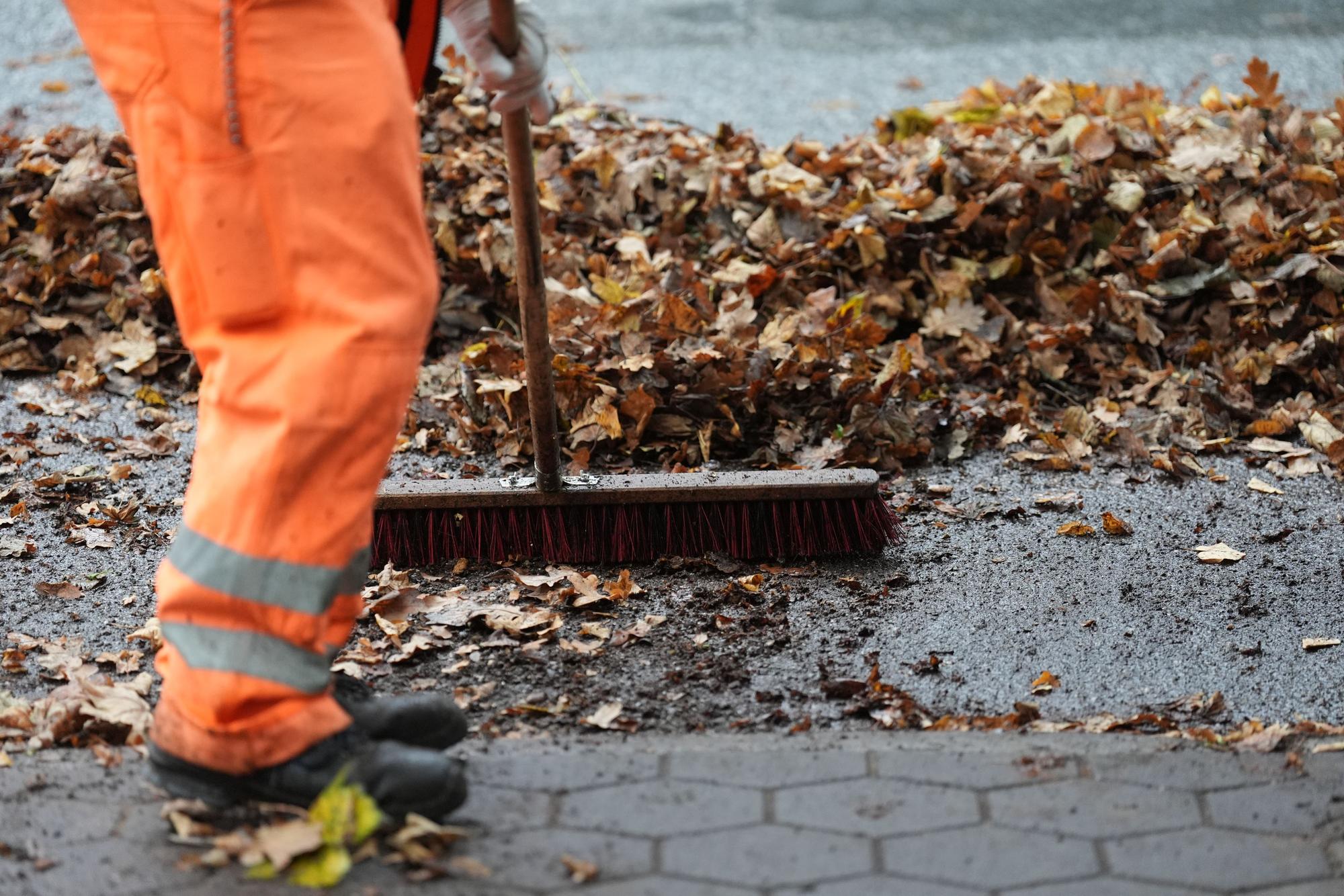 Ein Mitarbeiter der Stadtreinigung Hamburg (SRH) beseitigt das Laub mit Besen vom Gehweg