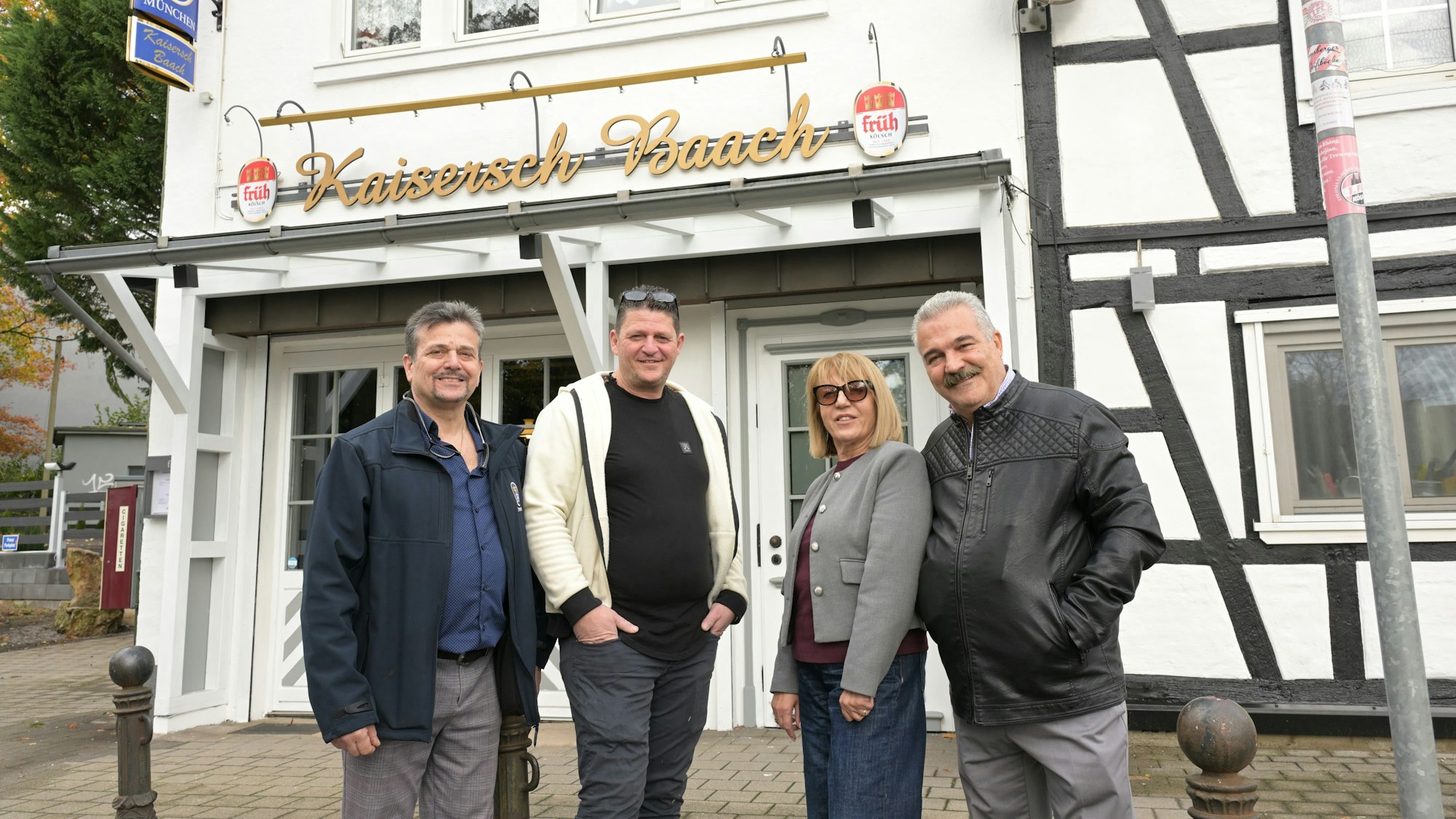 Drei Männer und eine Frau stehen vor einem Lokal mit der Aufschrift „Kaisersch Baach“.