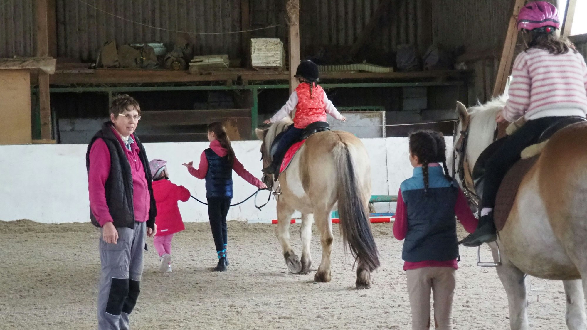 In der Reithalle steht Helga Lagier und schaut Kindern zu, die auf Pferden reiten lernen.