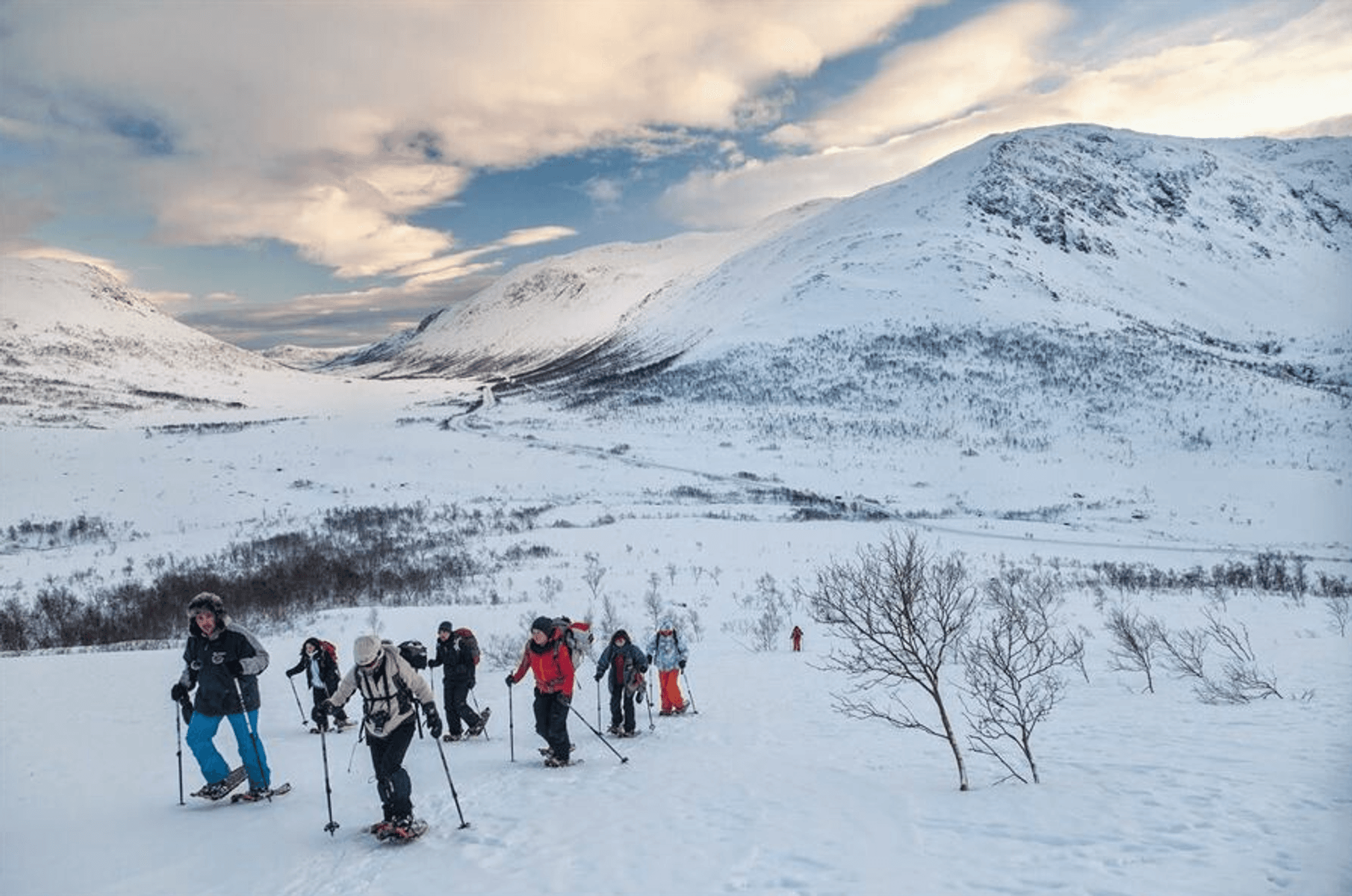 Das Bild zeigt eine Berglandschaft im Winter mit einer Gruppe von Personen auf einer Schneeschuhwanderung.