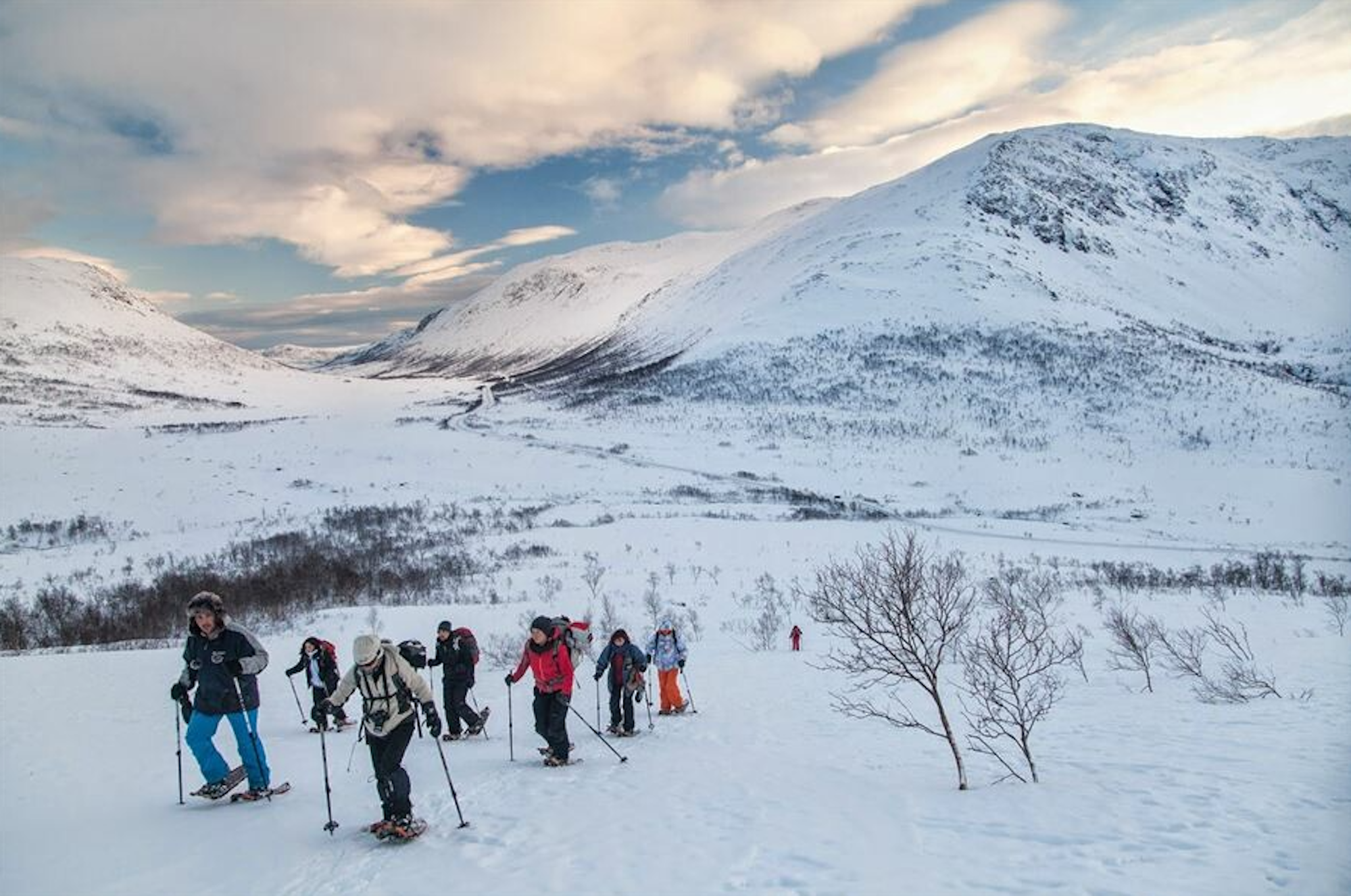Das Bild zeigt eine Berglandschaft im Winter mit einer Gruppe von Personen auf einer Schneeschuhwanderung.