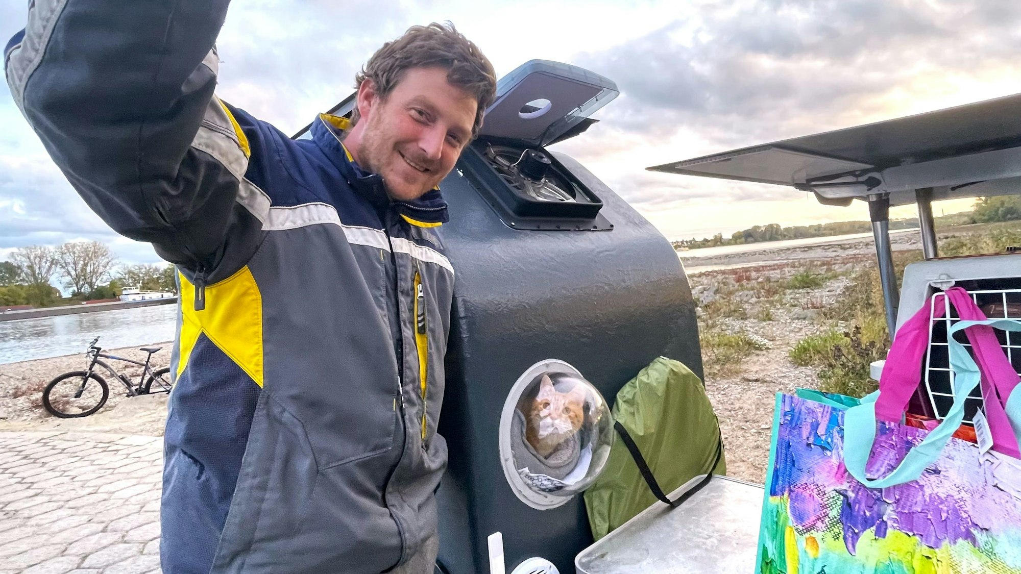 Ein Mann steht neben seinem Fahrrad-Anhänger, aus dem eine Katze schaut.