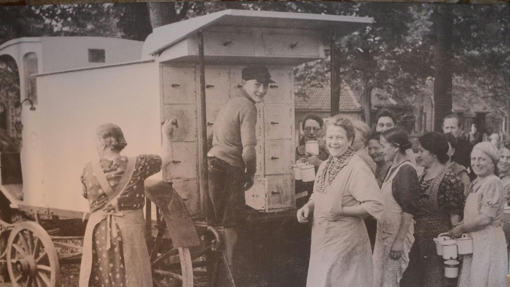Ein historisches Foto, Frauen stehen um einen Wagen mit Kastenaufbau herum.