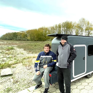 Zwei Männer vor ihren selbstgebauten Fahrradwohnwagen.