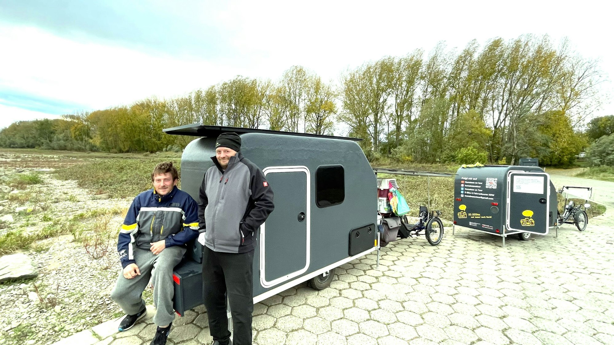 Zwei Männer vor ihren selbstgebauten Fahrradwohnwagen.
