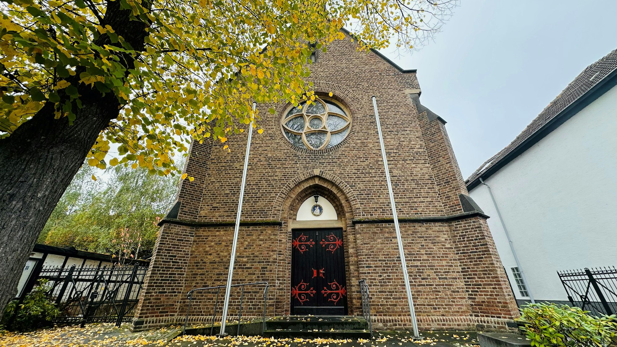 Zu sehen ist eine Kirche aus Stein, davor ein Baum.