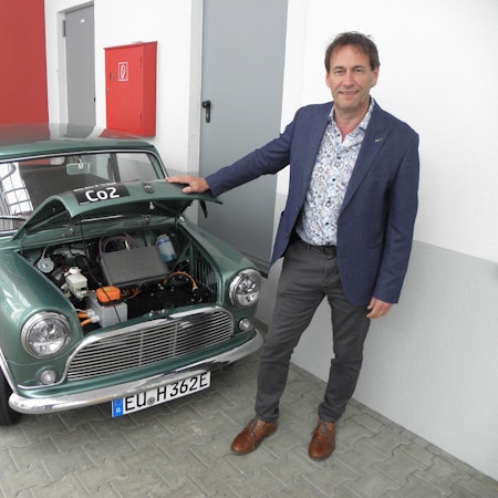 Kurt Heinen steht vor einem Mini Cooper mit geöffneter Motorhaube.