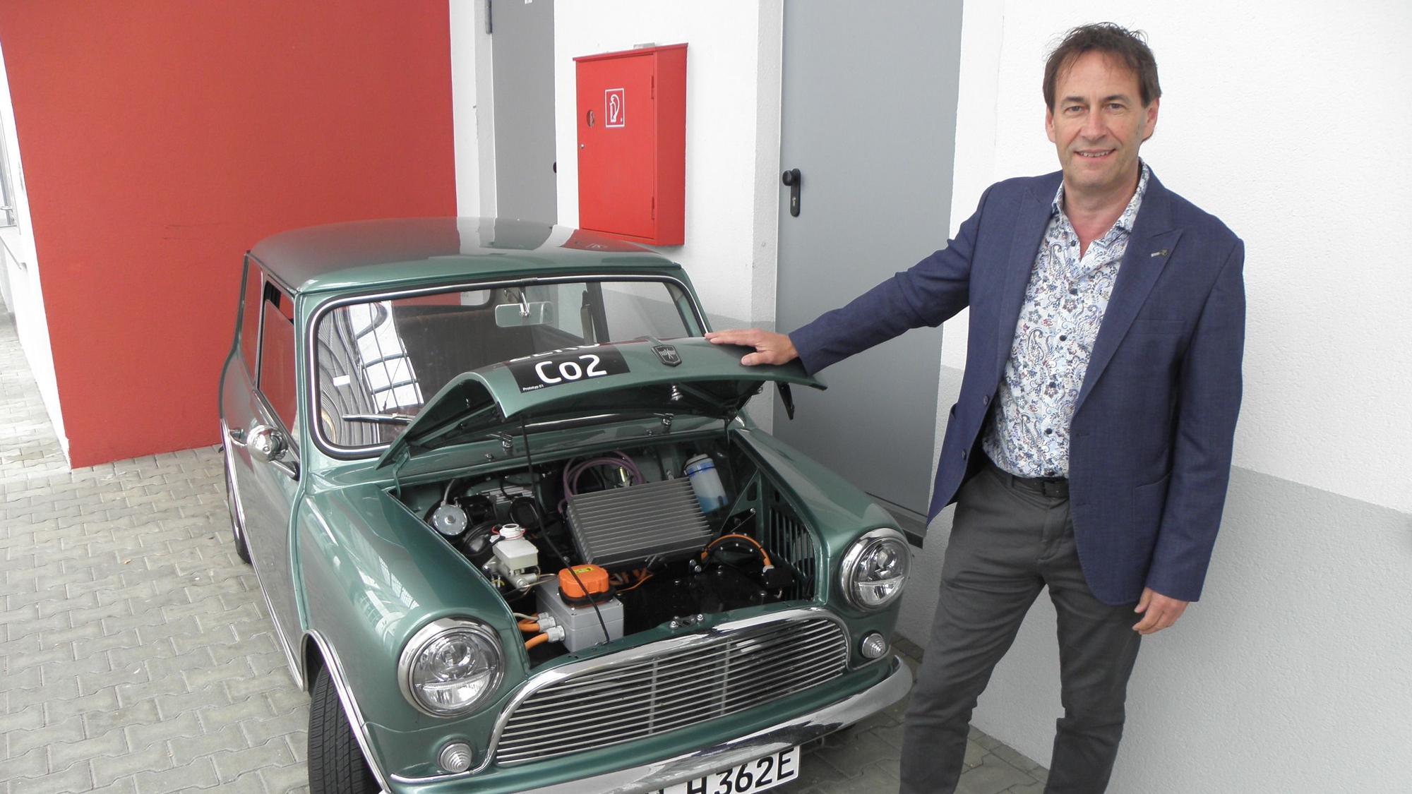 Kurt Heinen steht vor einem Mini Cooper mit geöffneter Motorhaube.