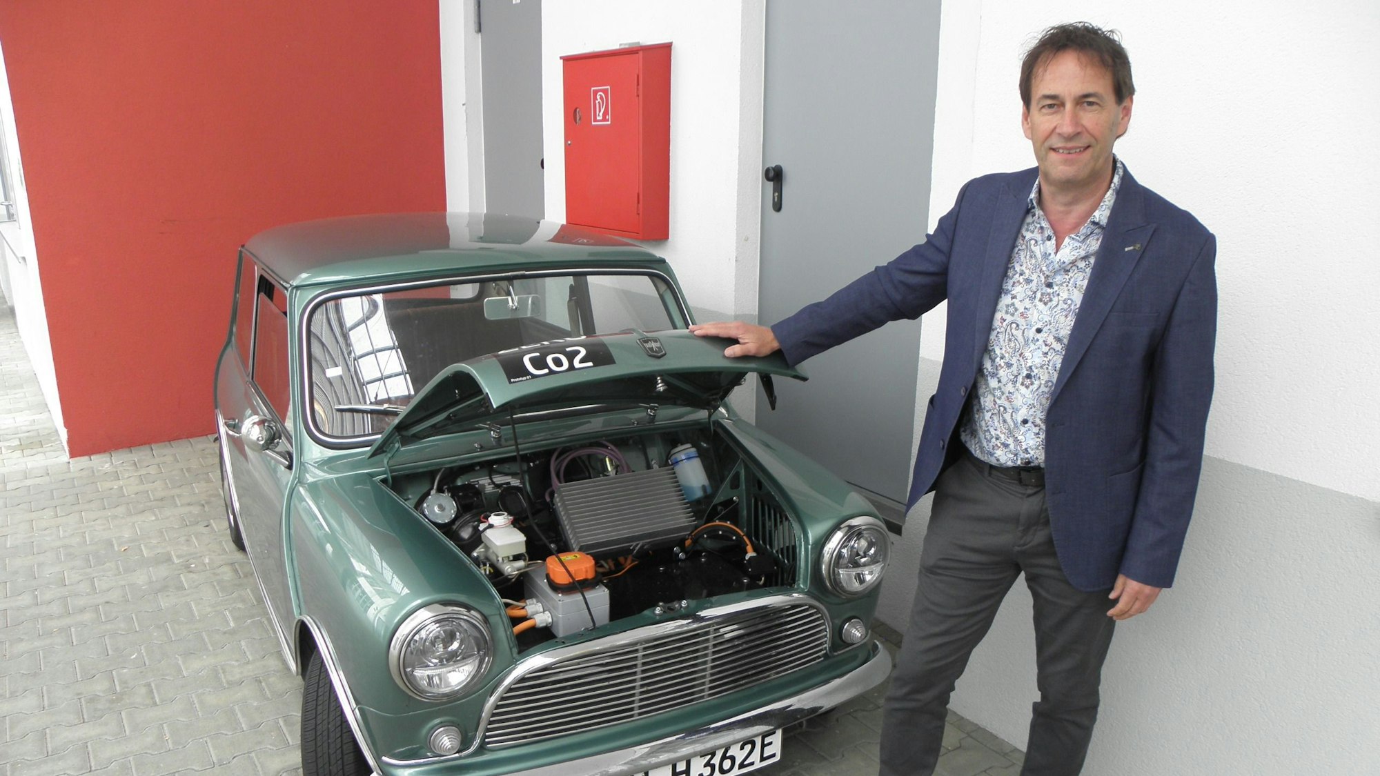 Kurt Heinen steht vor einem Mini Cooper mit geöffneter Motorhaube.