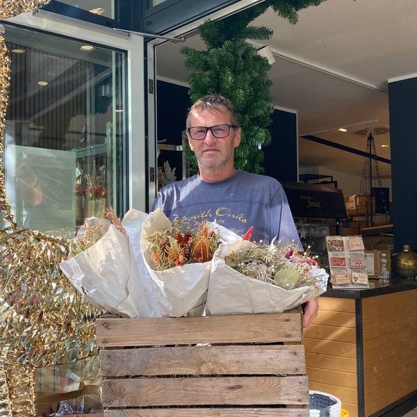 Zu sehen ist Dirk Jonas, der eine Holzkiste mit Blumengestecken trägt.