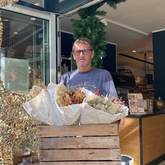 Zu sehen ist Dirk Jonas, der eine Holzkiste mit Blumengestecken trägt.