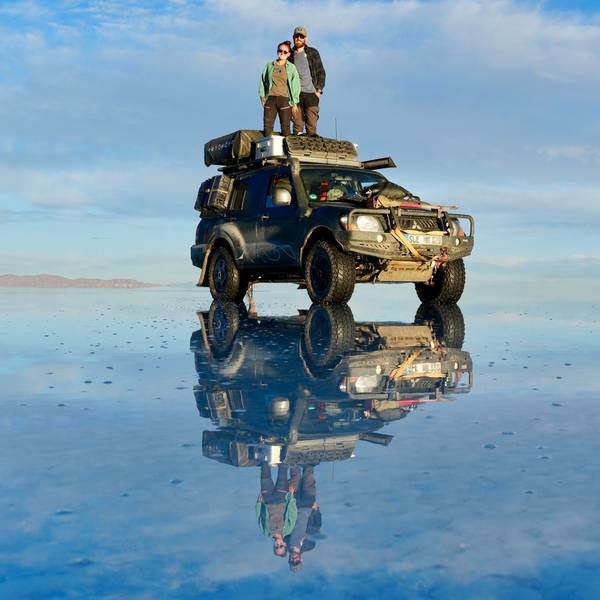 Rebecca und Marcel Schumacher stehen auf dem Dach ihres Mitsubishi Pajero, der sich auf einer Wasserfläche spiegelt.