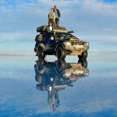 Rebecca und Marcel Schumacher stehen auf dem Dach ihres Mitsubishi Pajero, der sich auf einer Wasserfläche spiegelt.