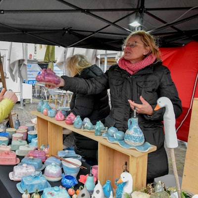 Zu sehen ist eine Frau, die an einem Stand mit Töpferware einkauft.