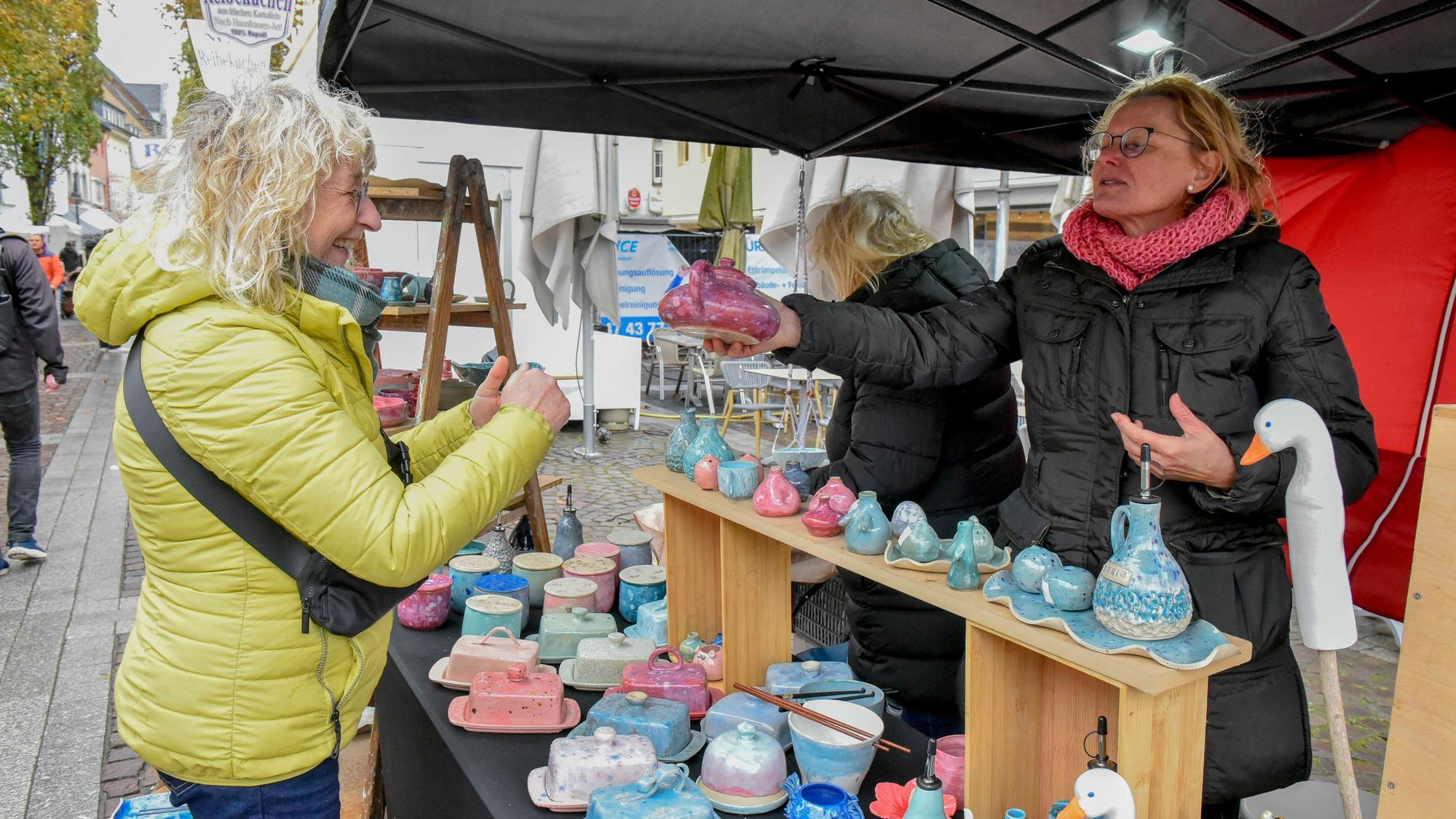 Zu sehen ist eine Frau, die an einem Stand mit Töpferware einkauft.