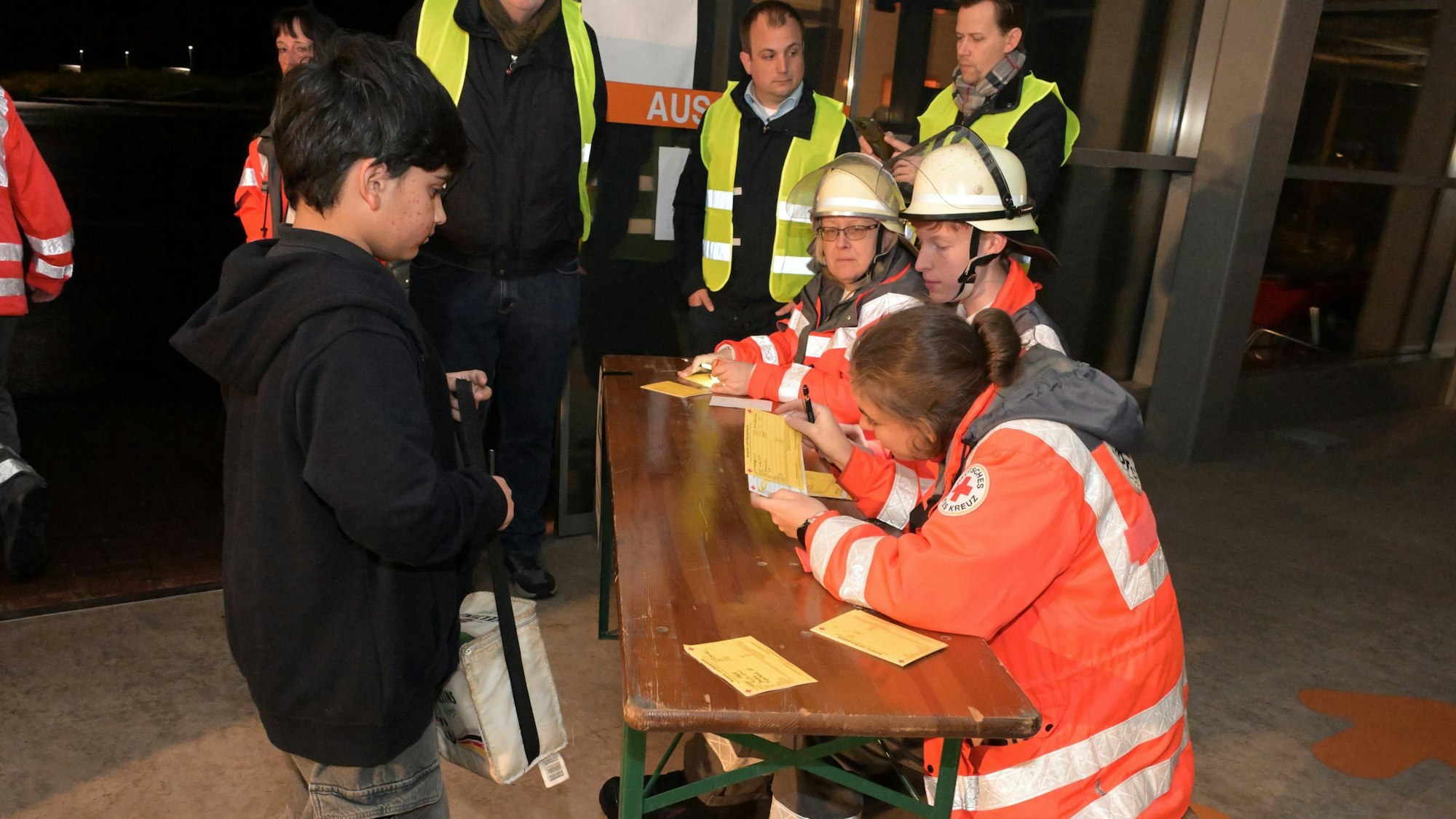 DRK-Einsatzkräfte sitzen an einem Tisch und registrieren in Sicherheit gebrachte Schüler.