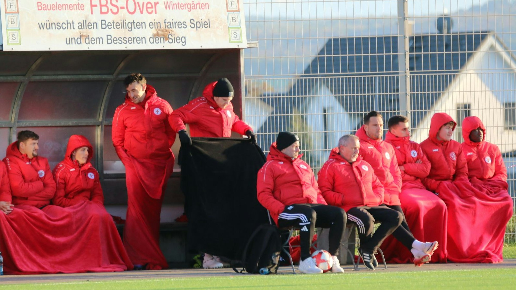 Die Auswechselspieler der Zülpicher sitzen unter wärmenden Decken. Trainer David Sasse breitet gerade eine Decke aus.