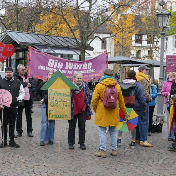 Menschen mit Protestplakaten und einem Transparent auf einem öffentlichen Platz.