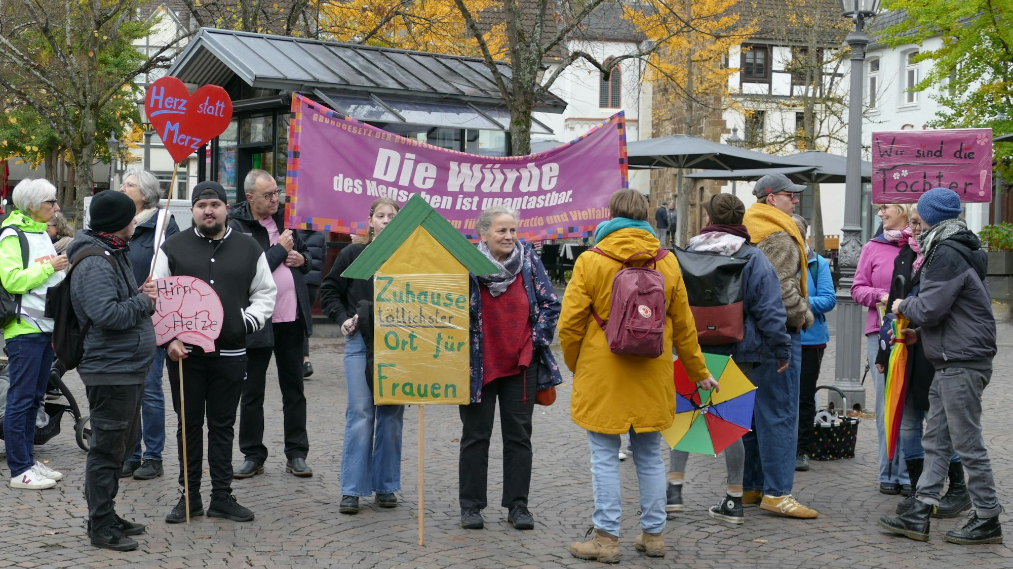 Menschen mit Protestplakaten und einem Transparent auf einem öffentlichen Platz.