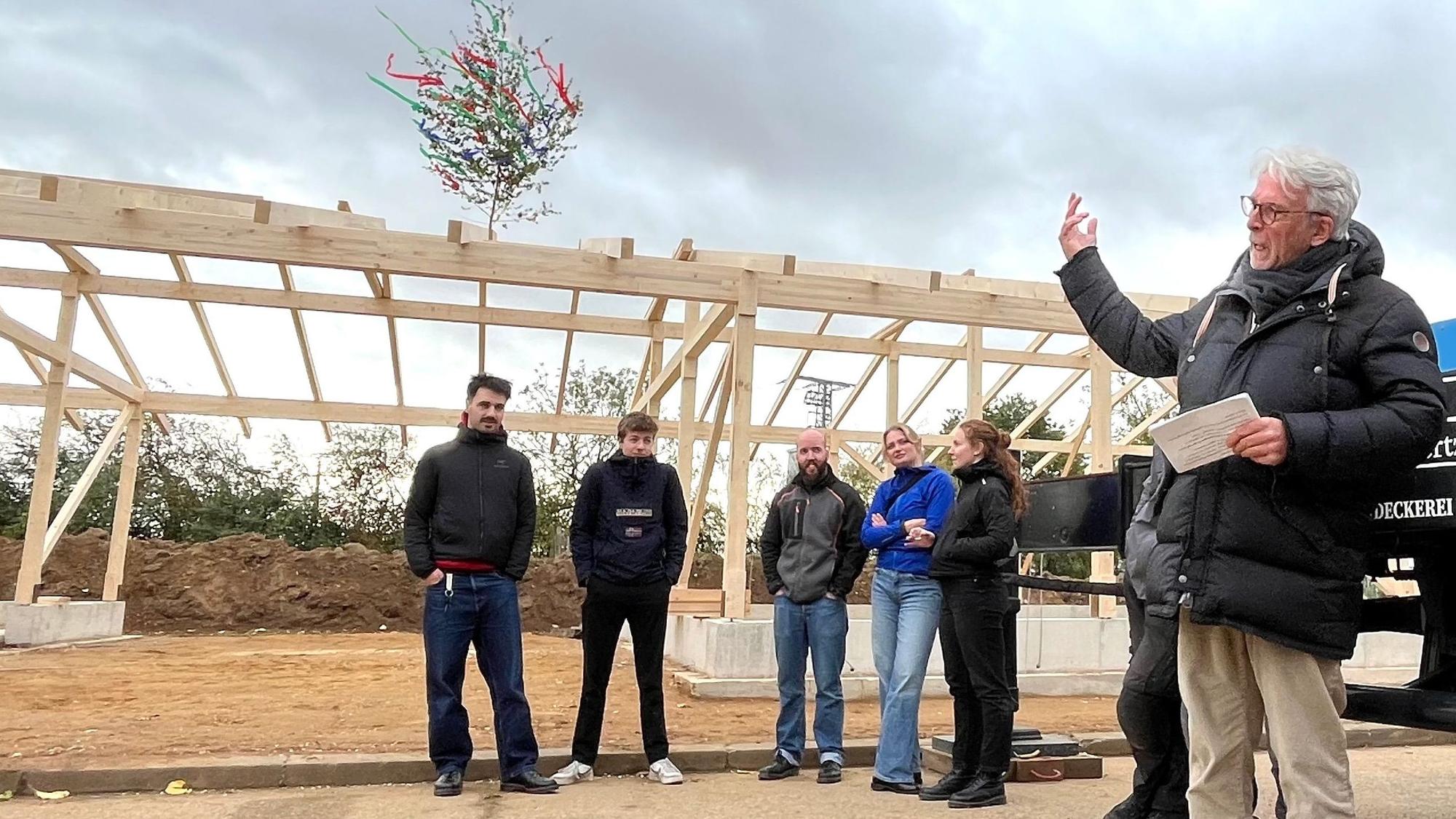Zu sehen ist eine Gruppe von Menschen. Im Hintergrund ist die Holzkonstruktion für den künftigen Stall zu erkennen.