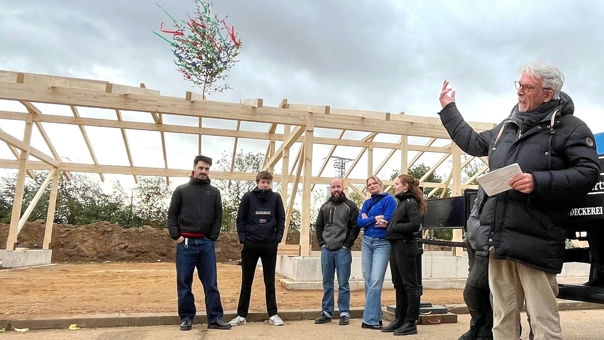 Zu sehen ist eine Gruppe von Menschen. Im Hintergrund ist die Holzkonstruktion für den künftigen Stall zu erkennen.