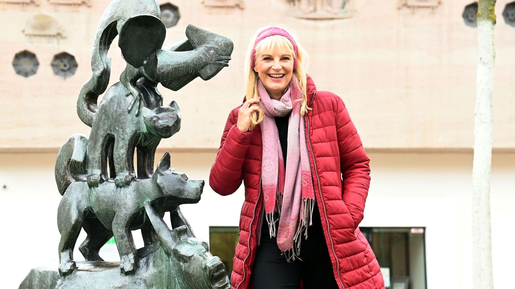 Eine Frau im roten Steppmantel steht neben einer Skulptur der Bremer Stadtmusikanten.
