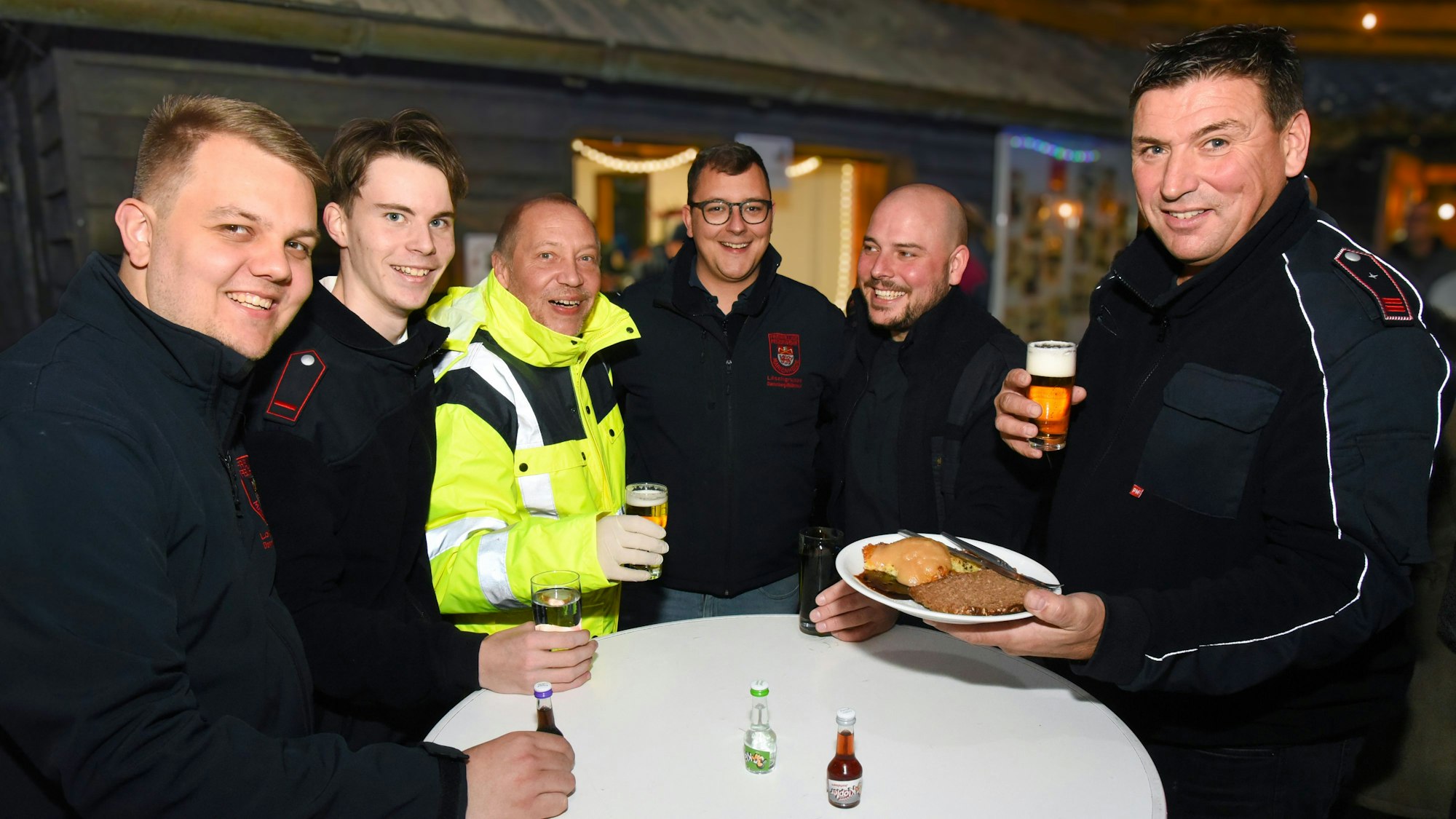 Feuerwehrmänner aus Dannenberg stehen am Tisch mit Bier und Reibekuchen in der Hand .