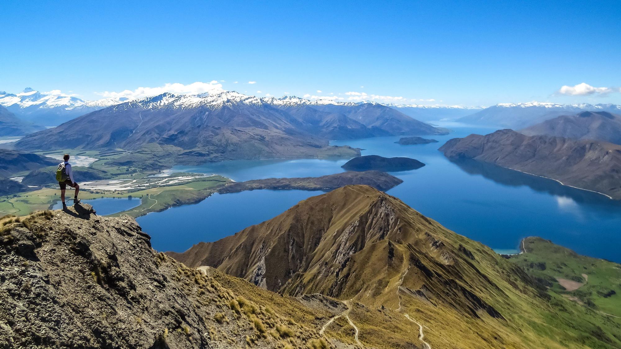 Ein Mann ist von hinten zu sehen, wie er auf eine Landschaft mit Seen und Bergen in Wanaka in Neuseeland schaut.