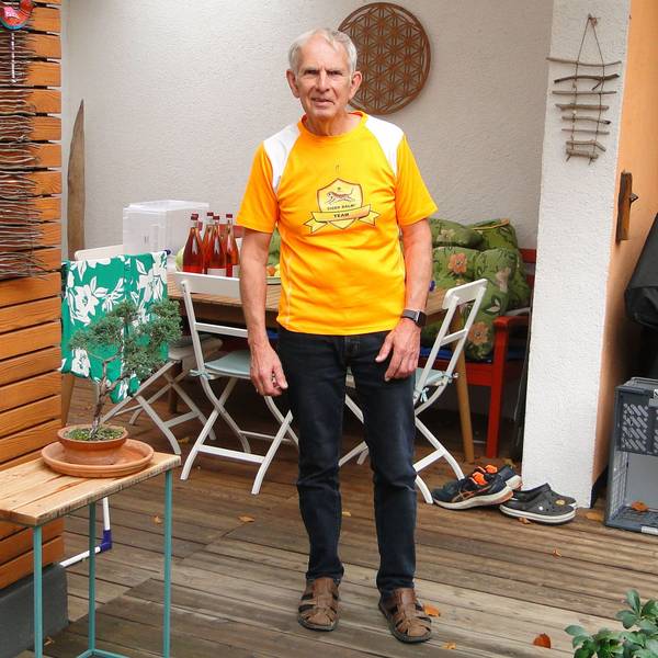 Ein Mann im orangen Shirt steht auf einer Terrasse.
