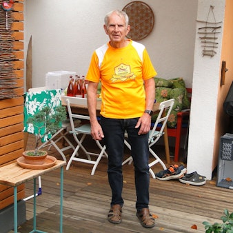 Ein Mann im orangen Shirt steht auf einer Terrasse.