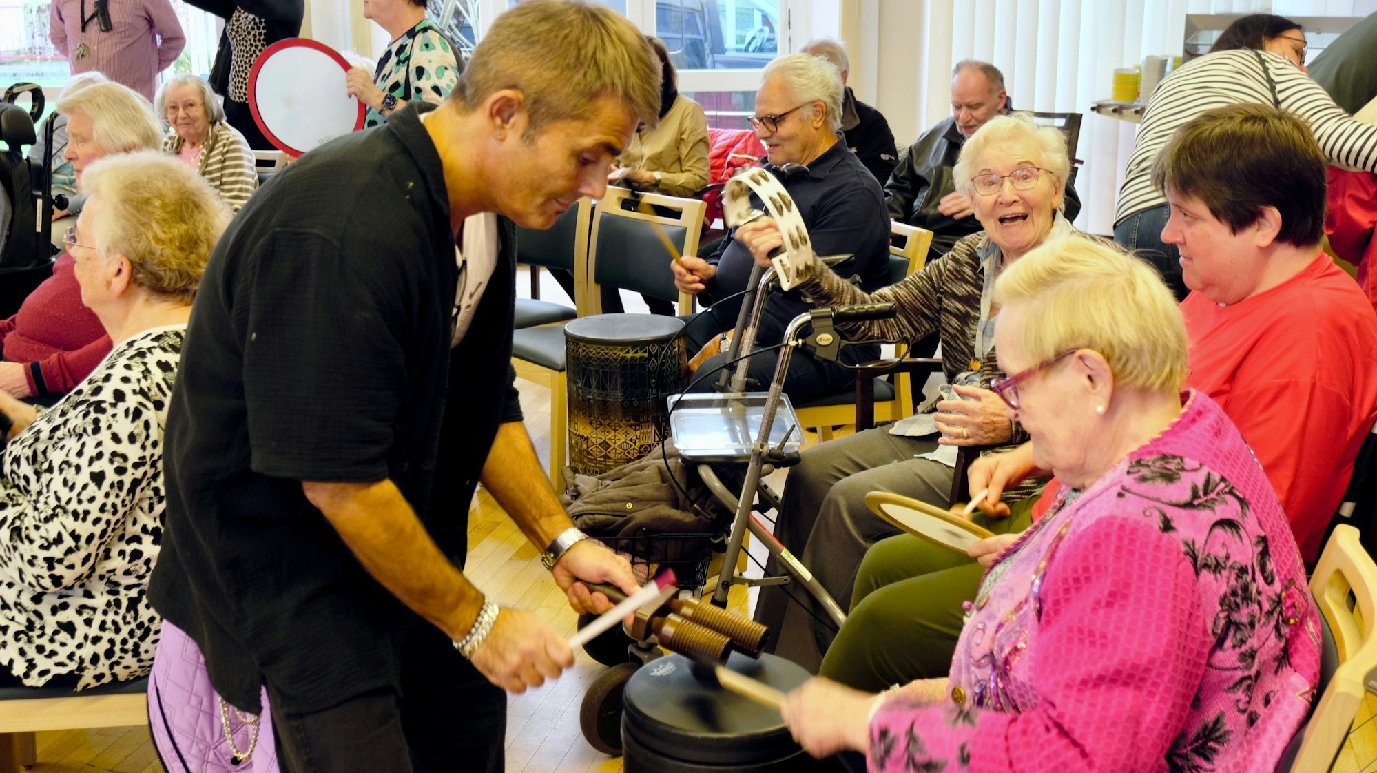 Ein junger Mann hilft einer Seniorin, die vor einer Trommel sitzt.