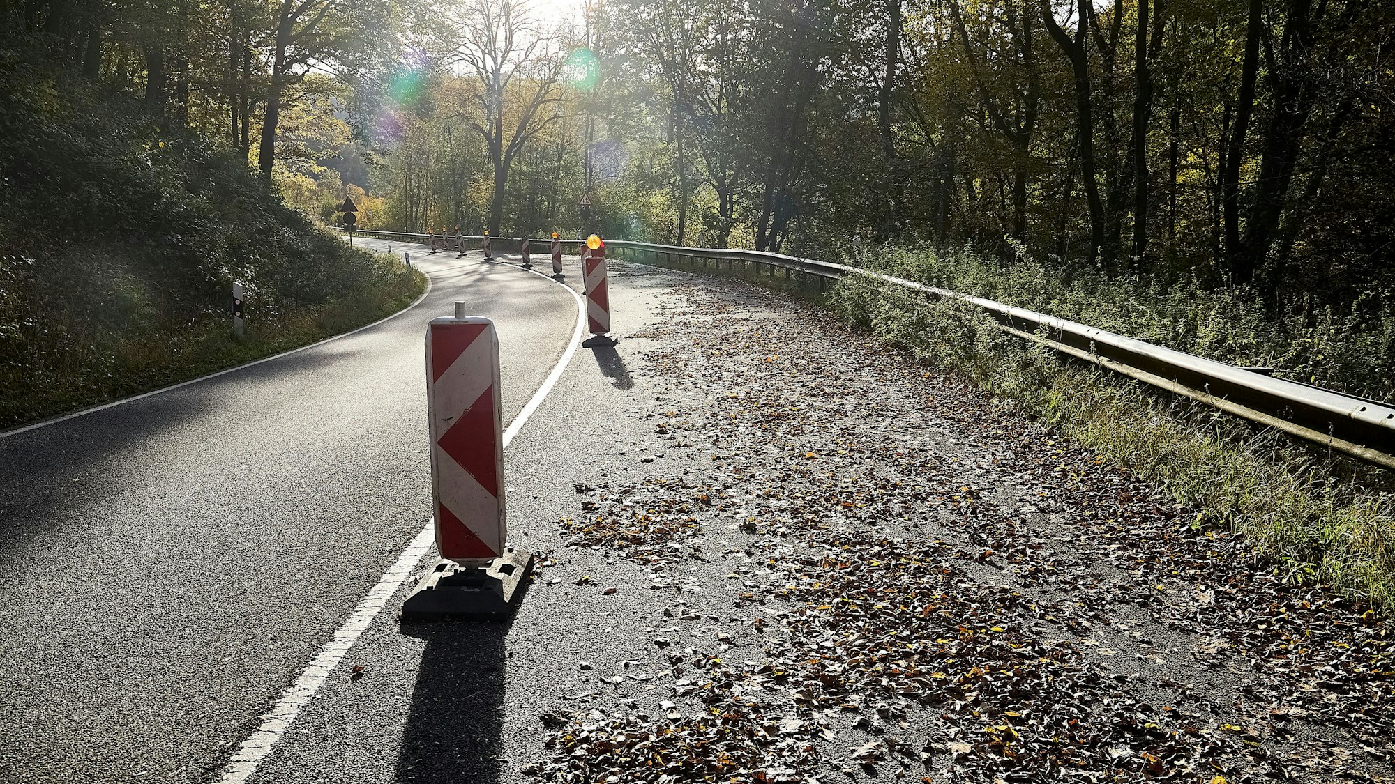 Die rechte Spur einer Straße ist mit Warnbaken abgesperrt. Auf der Fahrbahn liegt Laub.