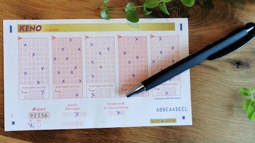 Auf einem Holztisch liegt ein Zettel, auf dem für das Gewinnspiel KENO Zahlen angekreuzt wurden.