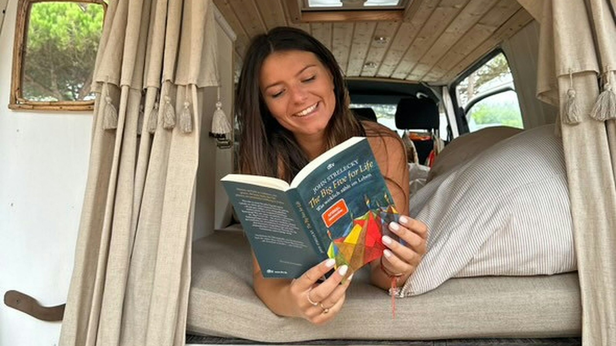 Anna Lüling liegt auf einer Matratze in einem Wohnwagen und hat das Buch „The Big Five for Life“ des Autors John Strelecky aufgeschlagen.