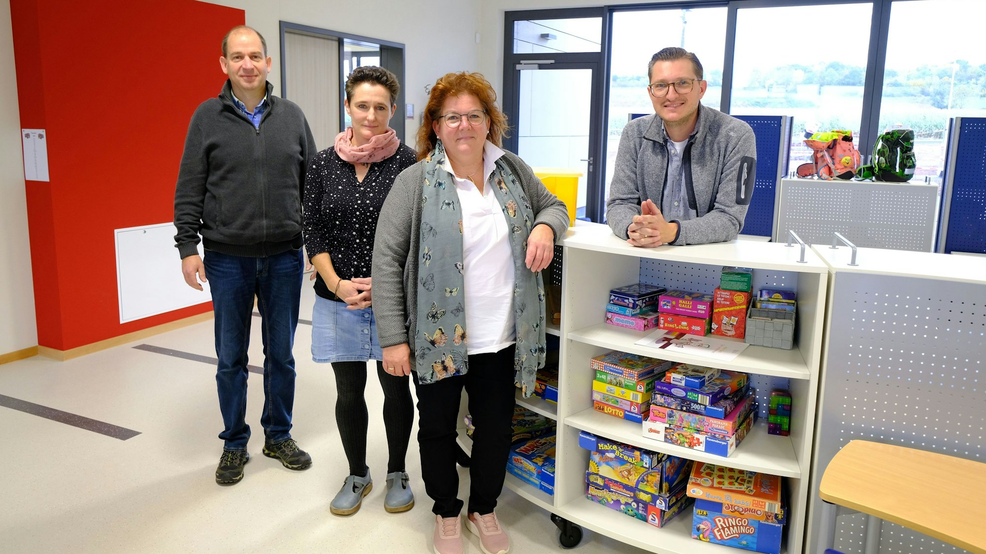 Zwei Frauen und zwei Männer stehen an einem Regal in der offenen Lernlandschaft der Gemeinschaftsgrundschule Firmenich-Obergartzem.