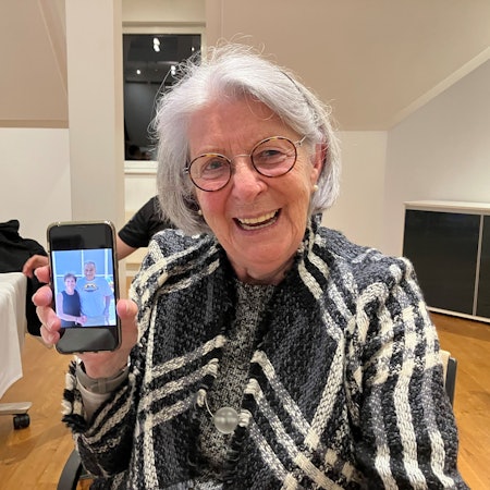 Eine ältere Dame zeigt ein Foto mit zwei Personen auf ihrem Handy.