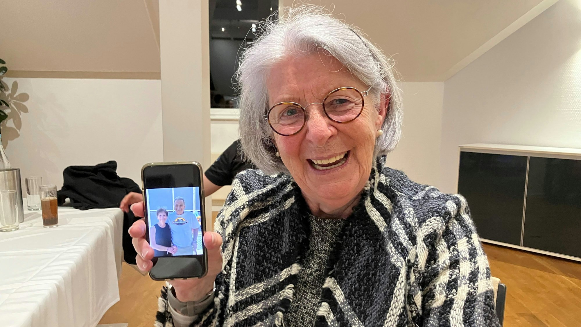 Eine ältere Dame zeigt ein Foto mit zwei Personen auf ihrem Handy.