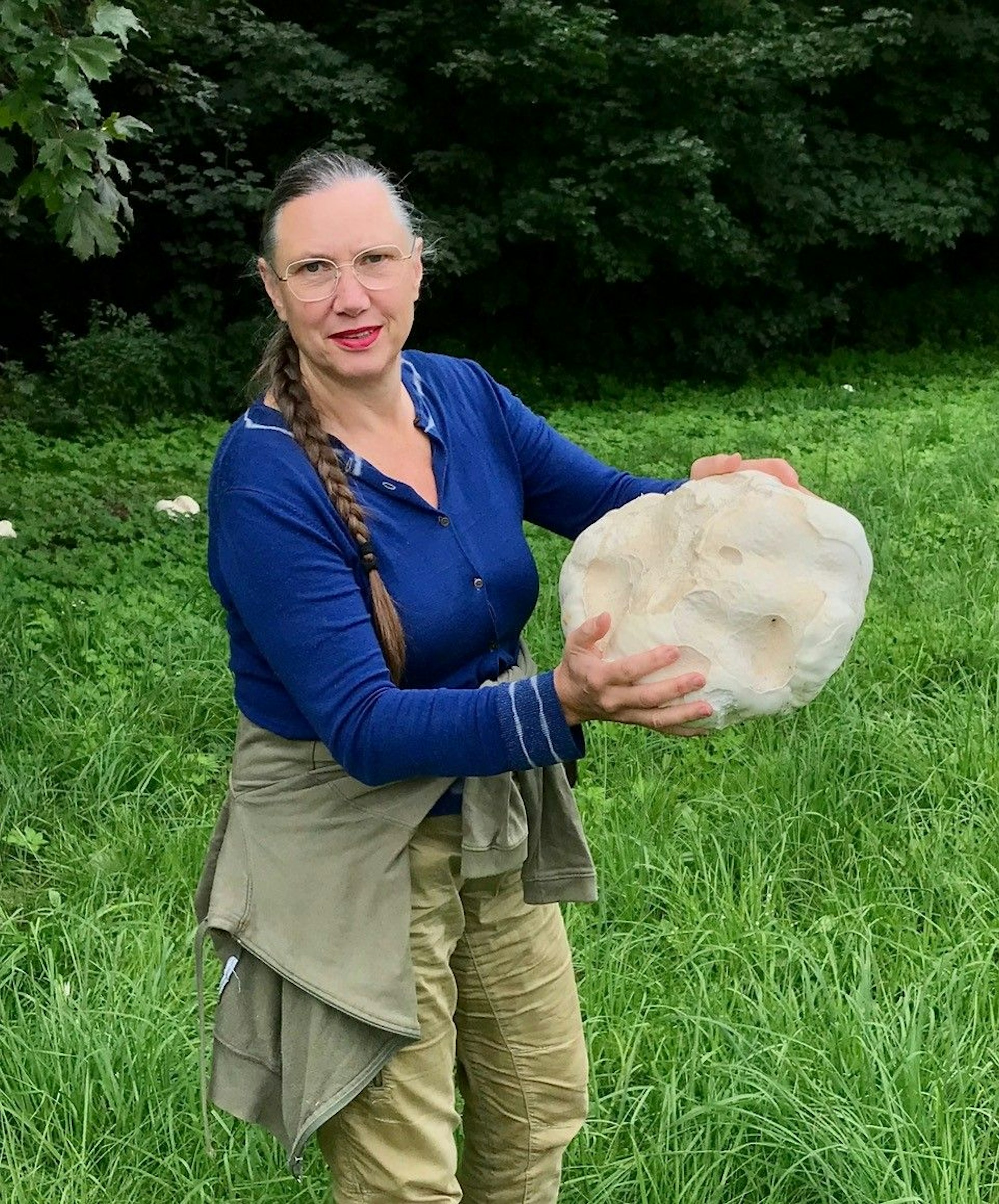 Eine Frau mit Zopf und Brille hält einen großen Stein in der Hand.