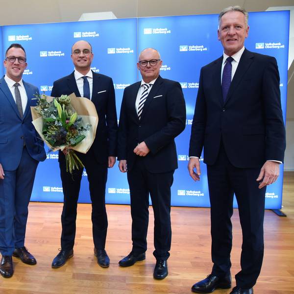 Fünf Herren im Anzug, der Mann in der Mitte hält einen Blumenstrauß.