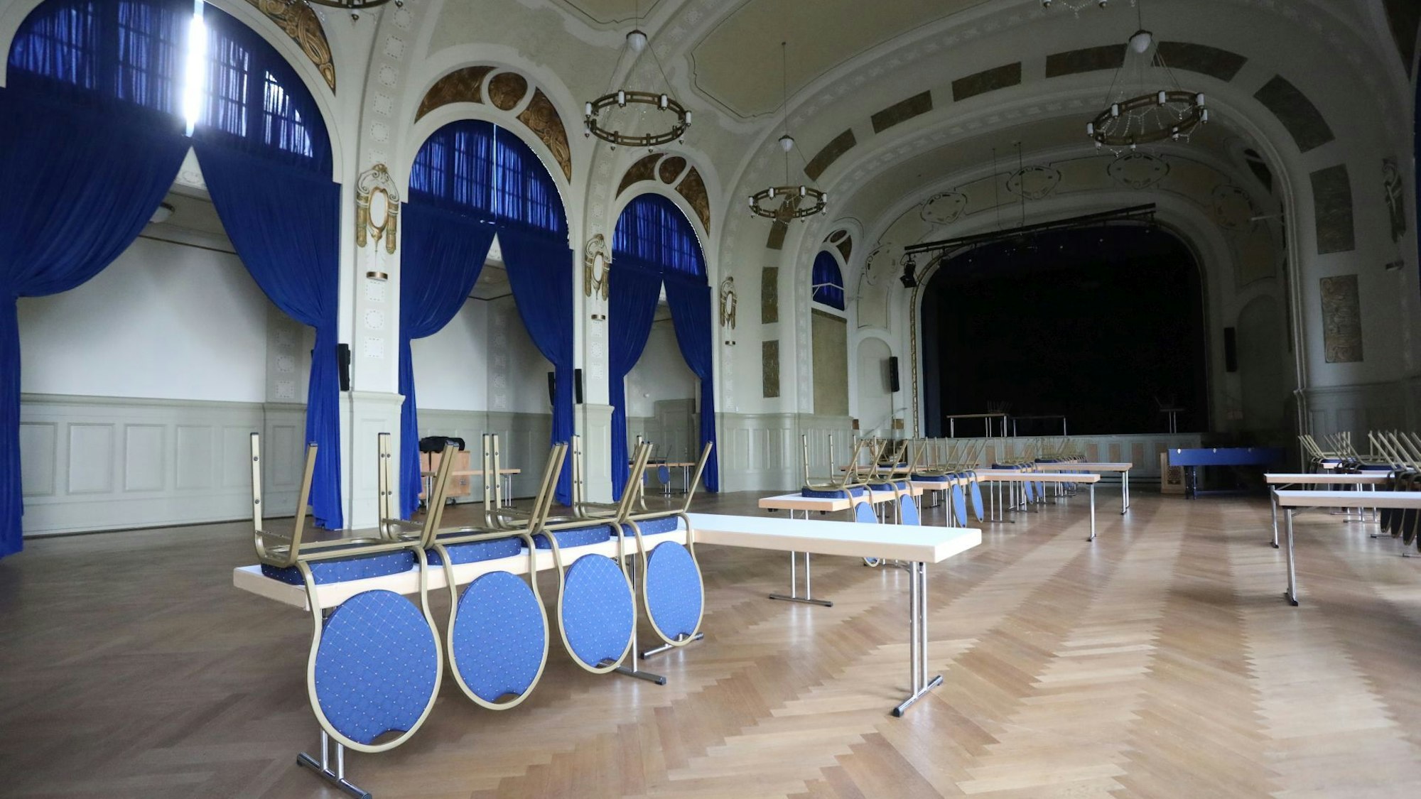 In einem Veranstaltungsaal stehen Tische, auf denen zum Teil Stühle liegen.