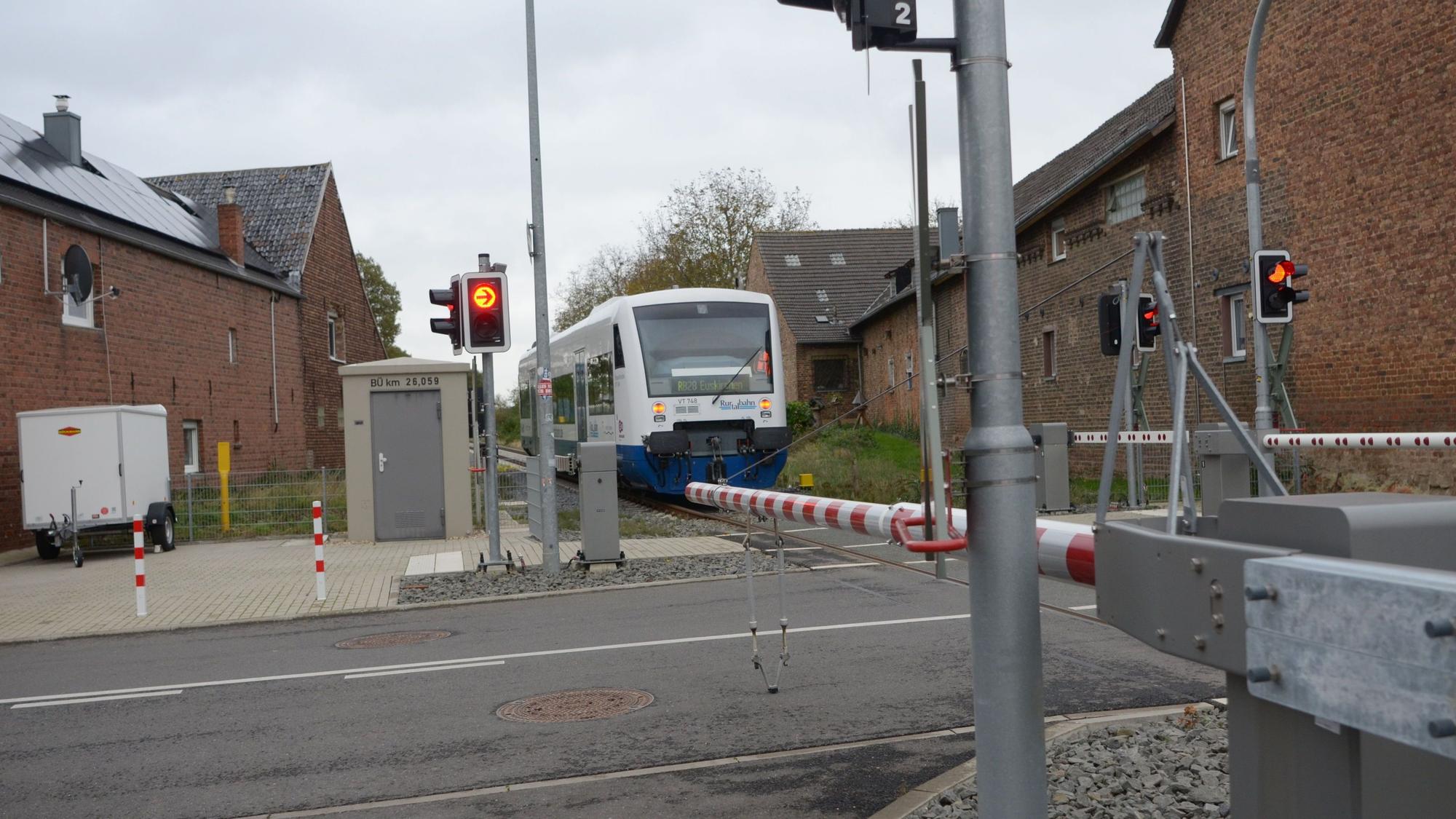 Das Bild zeigt einen geschlossenen Bahnübergang in Elsig, dem sich ein Zug nähert.