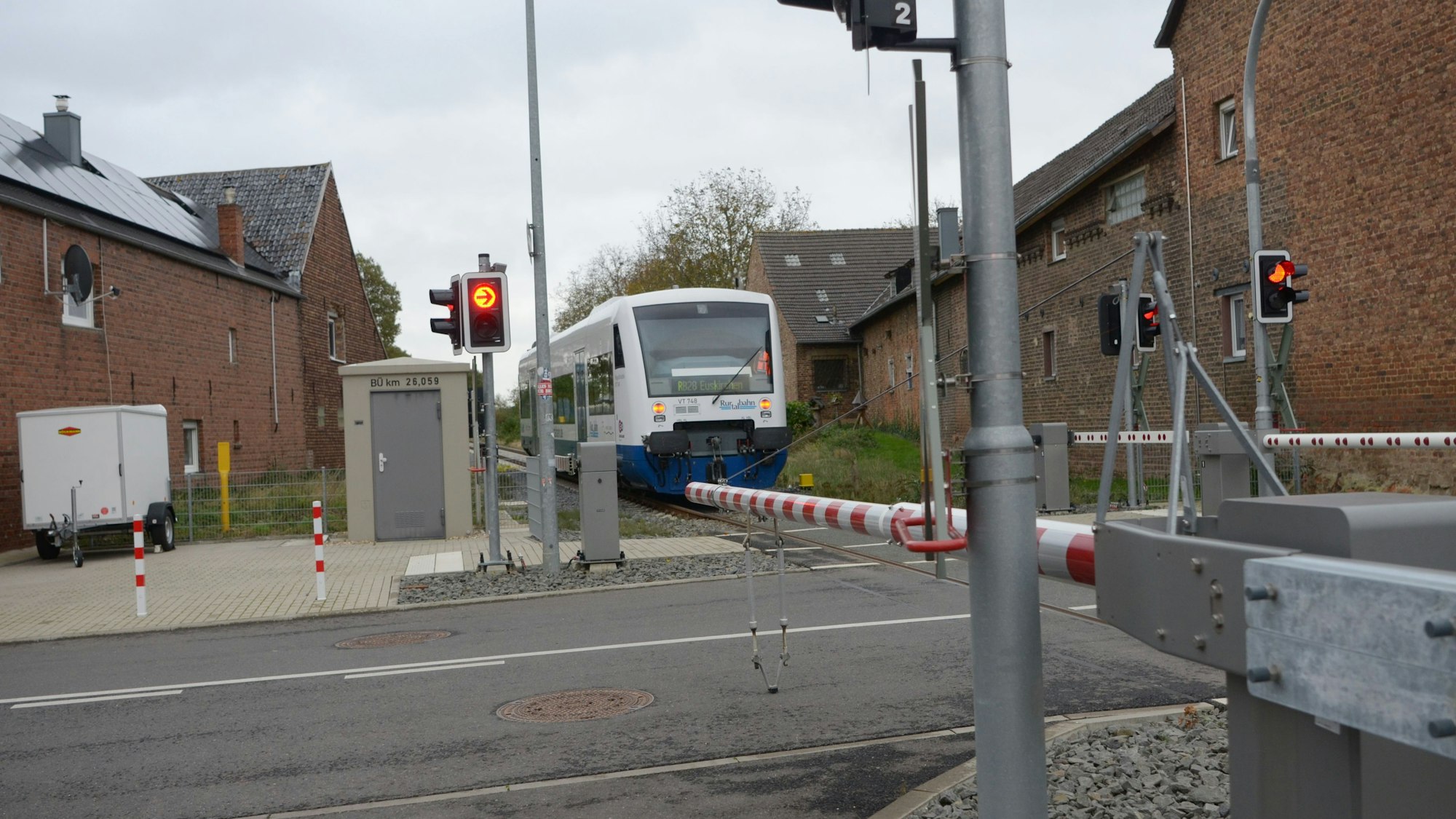 Das Bild zeigt einen geschlossenen Bahnübergang in Elsig, dem sich ein Zug nähert.