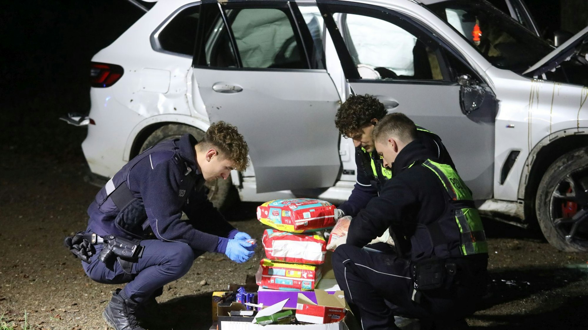 Drei Polizisten hocken auf dem Boden und sichten das gefundene Material aus dem BMW.