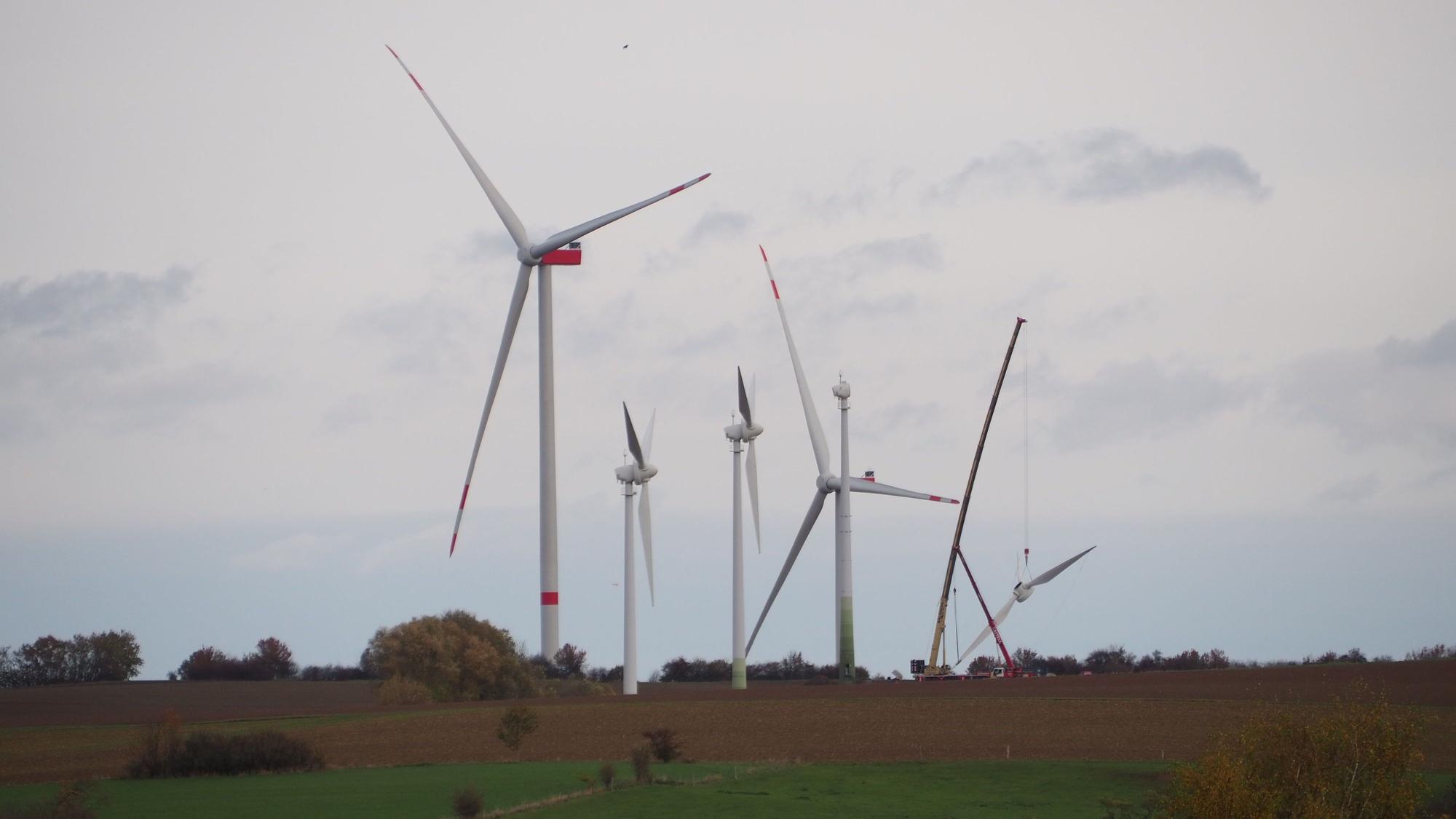Auf einem Hügel stehen mehrere Windräder. Eines wird gerade demontiert, der Rotor hängt am Kranhaken.
