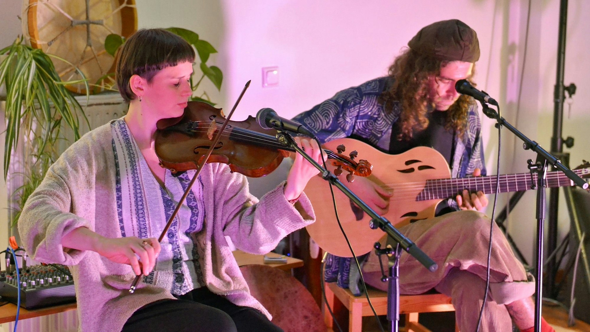 Eine Violinistin und ein Gitarrist spielen ihre Instrumente im Sitzen.