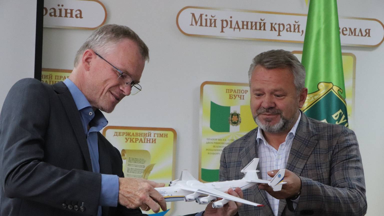 Der scheidende Bürgermeister von Bergisch Gladbach, Frank Stein, und der Bürgermeister der Stadt Butscha, Anatolii Fedoruk, stehen nebeneinander und halten gemeinsam ein Modellflugzeug. Beide lächeln leicht.