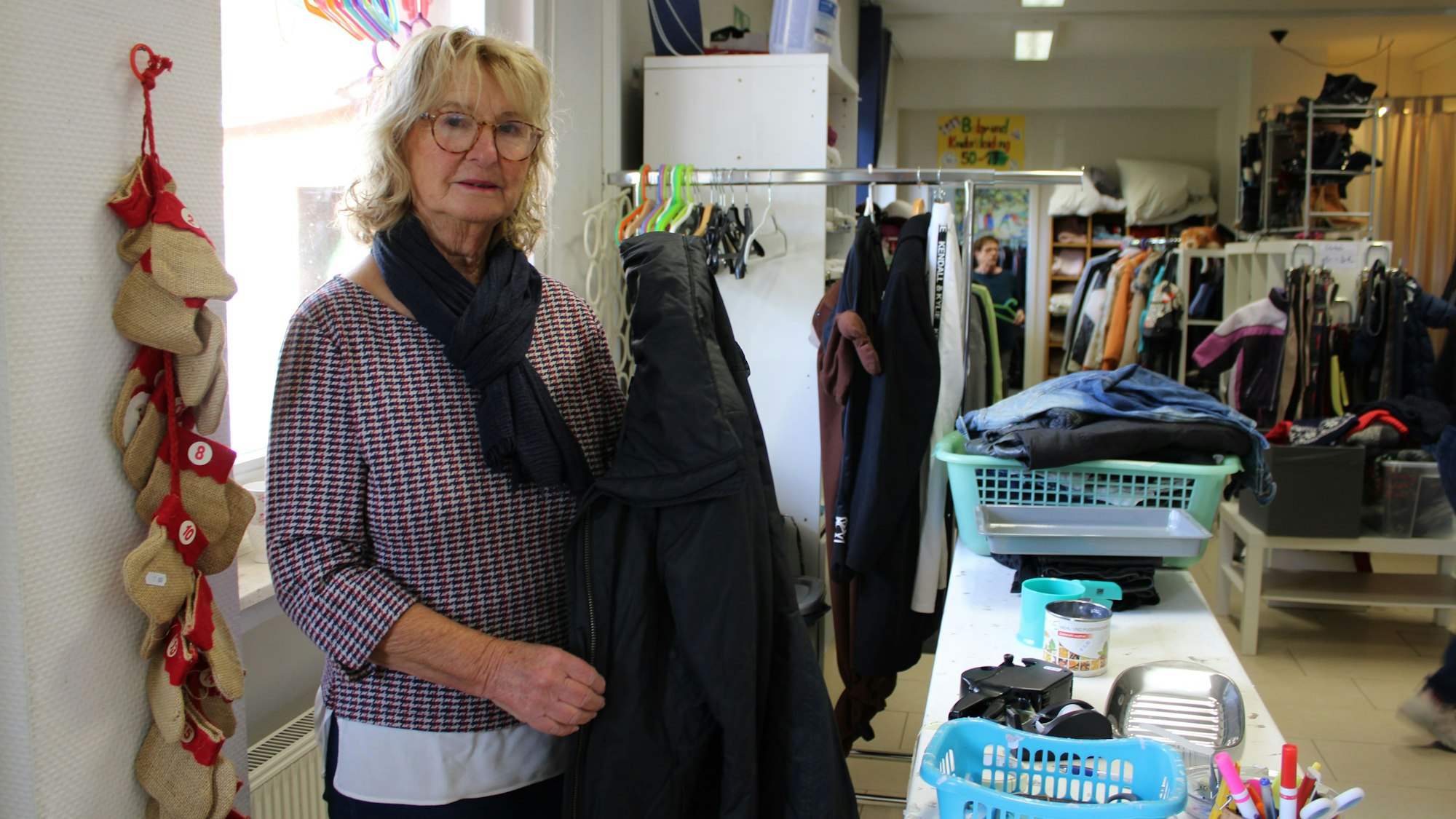 Eine Frau steht in einem Second Hand Laden und hält einen Mantel.
