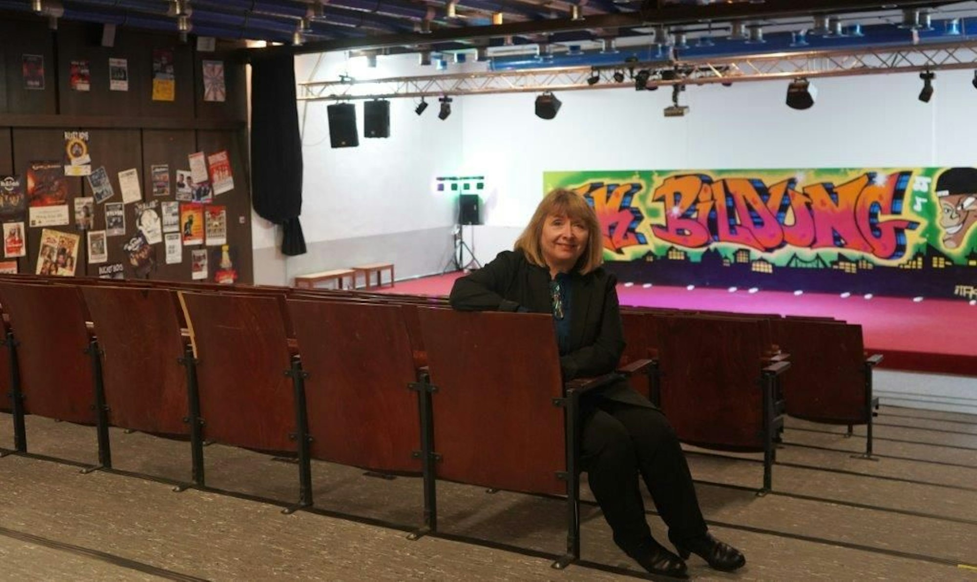 Eine Frau sitzt in einem Kino, im Hintergrund ist die Bühne, wo auch die traditionelle Karnevalssitzung stattfindet.