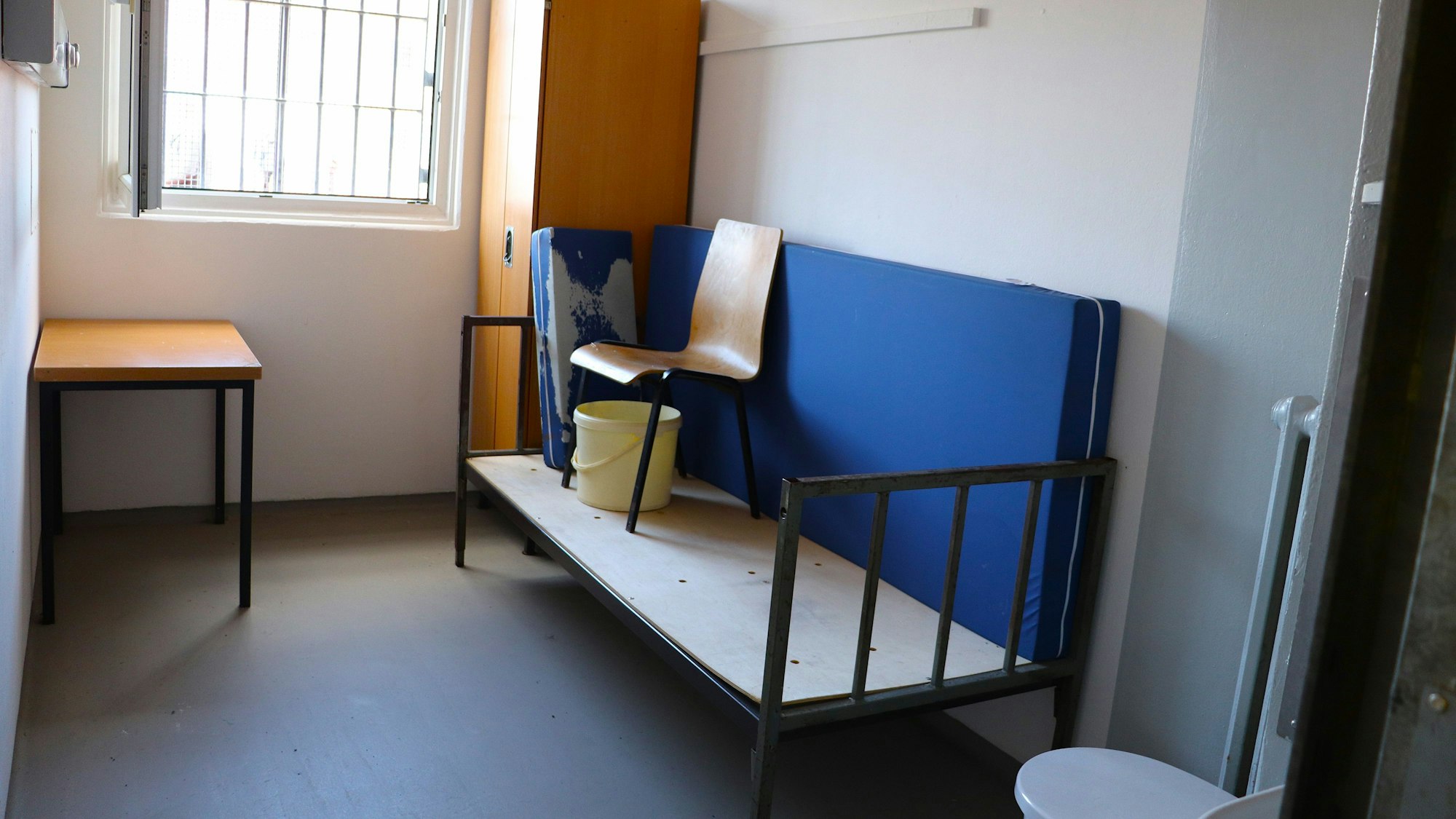 In einer Gefängniszelle steht einfaches Mobiliar und eine Toilette.